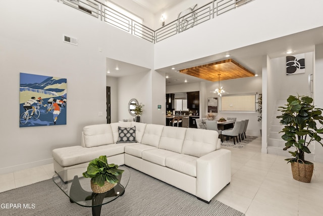 living area with a notable chandelier, light tile patterned floors, visible vents, a high ceiling, and baseboards