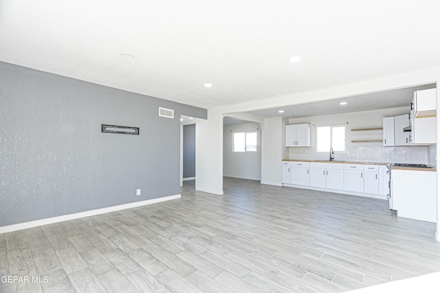 unfurnished living room with light wood finished floors, baseboards, visible vents, a sink, and recessed lighting