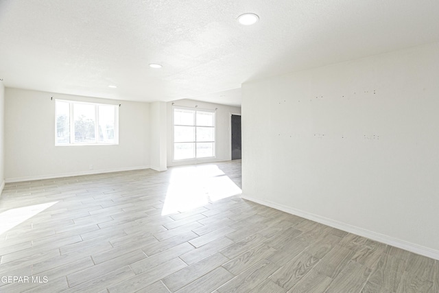 unfurnished room with a textured ceiling, recessed lighting, light wood-style flooring, and baseboards