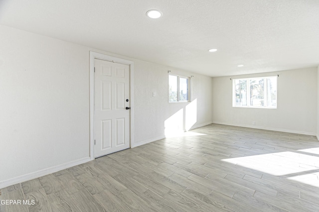 spare room featuring a textured ceiling, light wood finished floors, recessed lighting, and baseboards