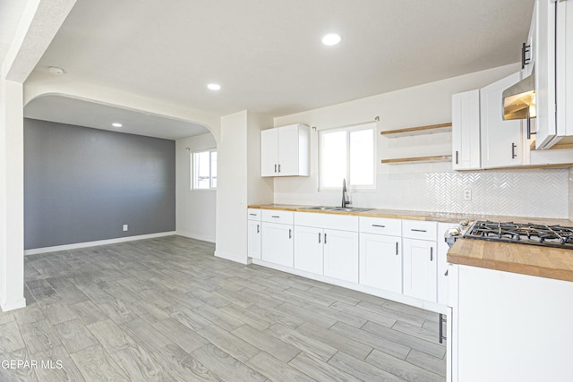 kitchen with butcher block countertops, white cabinetry, and a sink