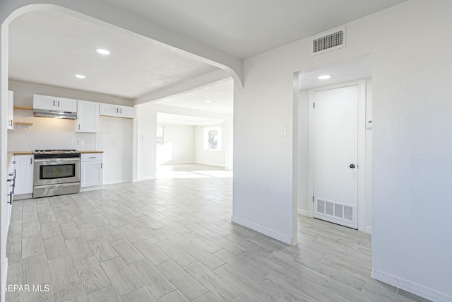 kitchen featuring stainless steel gas range oven, visible vents, white cabinets, under cabinet range hood, and open shelves