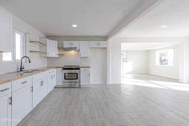 kitchen with open shelves, white cabinetry, a sink, under cabinet range hood, and stainless steel gas range oven