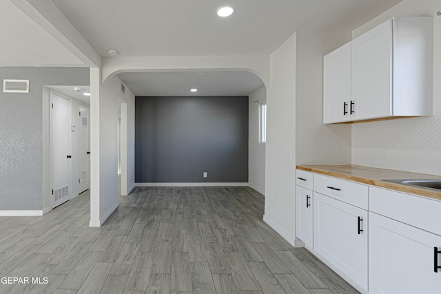 kitchen featuring arched walkways, butcher block counters, visible vents, light wood-style flooring, and white cabinetry