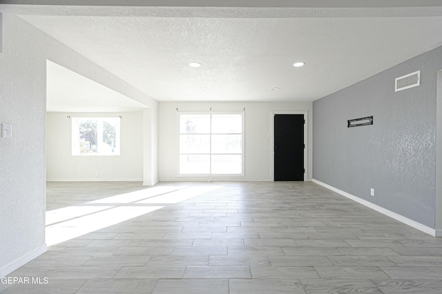 empty room featuring baseboards, visible vents, a textured ceiling, and a textured wall