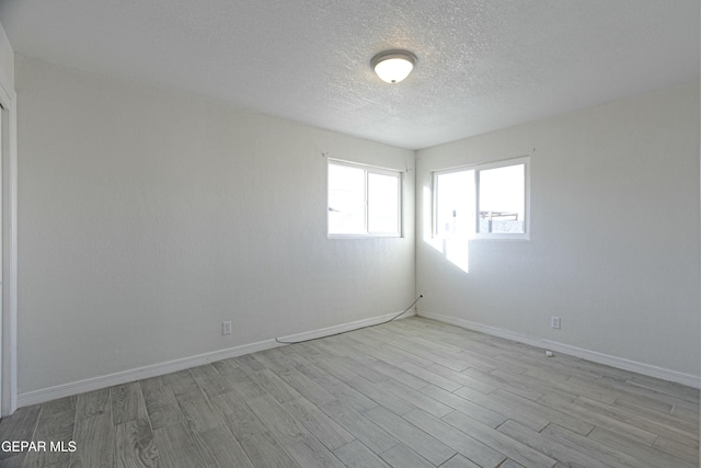 spare room with light wood-style flooring, baseboards, and a textured ceiling