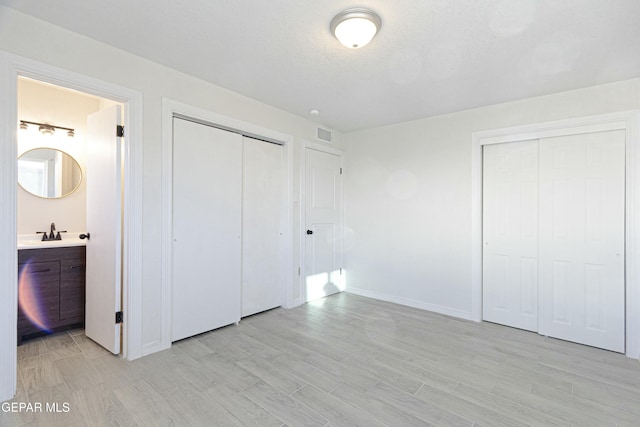 unfurnished bedroom featuring a sink, two closets, visible vents, light wood finished floors, and ensuite bath