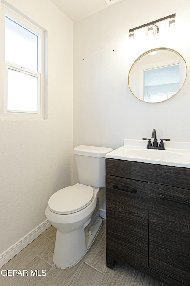 half bathroom featuring baseboards, vanity, and toilet