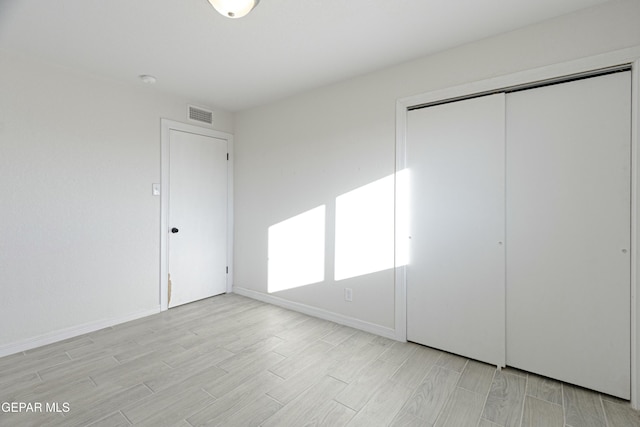 unfurnished bedroom featuring wood finish floors, a closet, visible vents, and baseboards