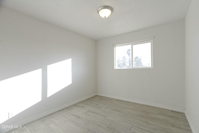 unfurnished room featuring baseboards, a textured ceiling, and light wood finished floors