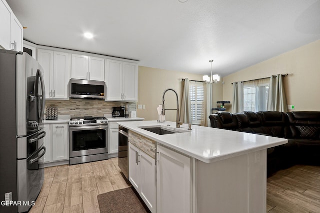 kitchen featuring a kitchen island with sink, stainless steel appliances, open floor plan, hanging light fixtures, and light countertops