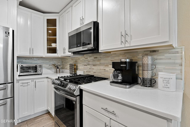 kitchen with white cabinetry, light countertops, appliances with stainless steel finishes, tasteful backsplash, and glass insert cabinets