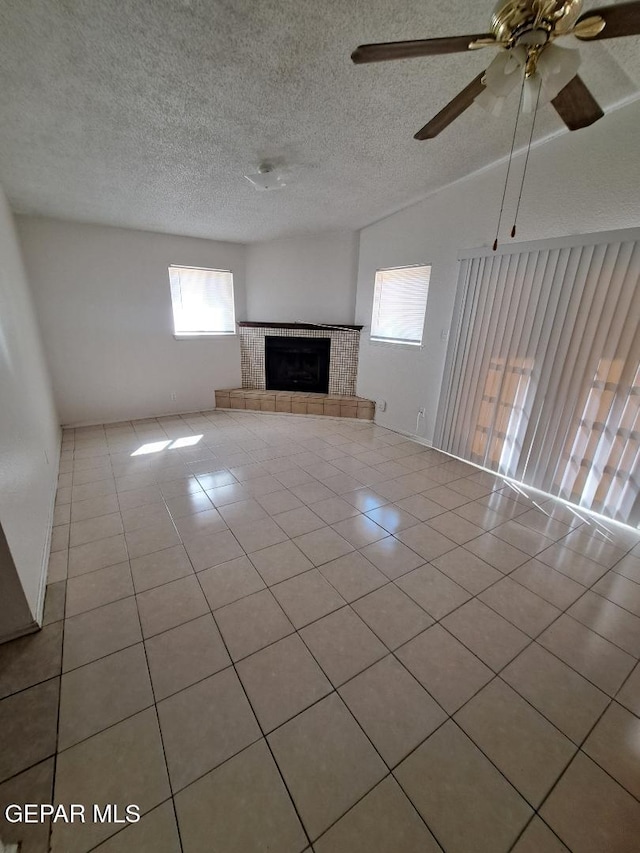 unfurnished living room with a ceiling fan, a tile fireplace, light tile patterned flooring, and a textured ceiling