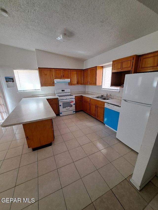 kitchen featuring white appliances, brown cabinetry, a kitchen island, light countertops, and a sink