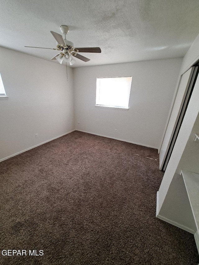 spare room featuring ceiling fan, dark colored carpet, and a textured ceiling