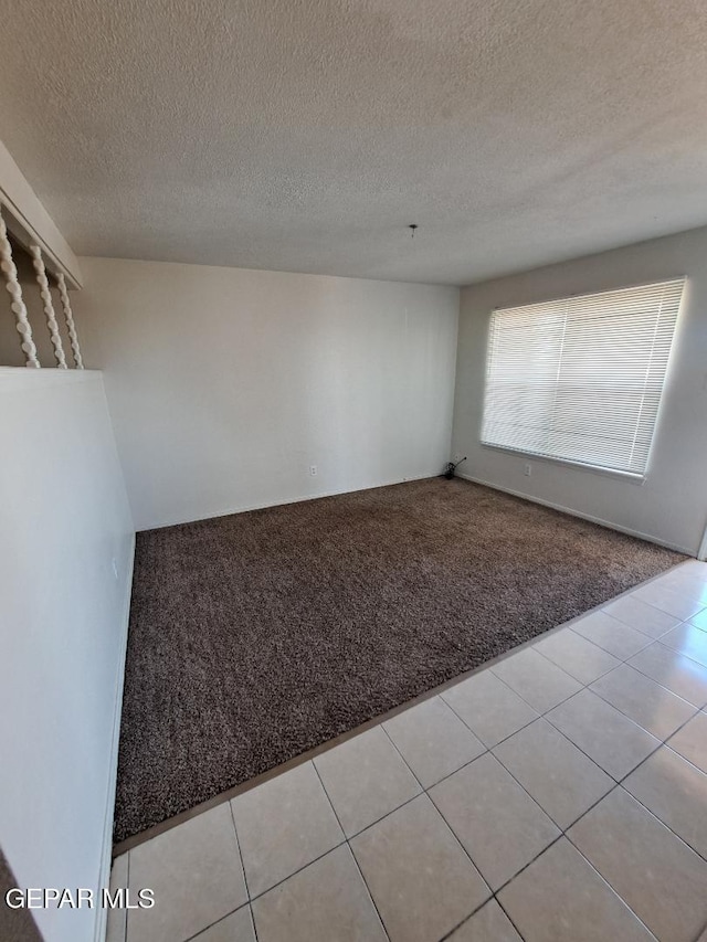 empty room with light tile patterned floors, a textured ceiling, and light colored carpet