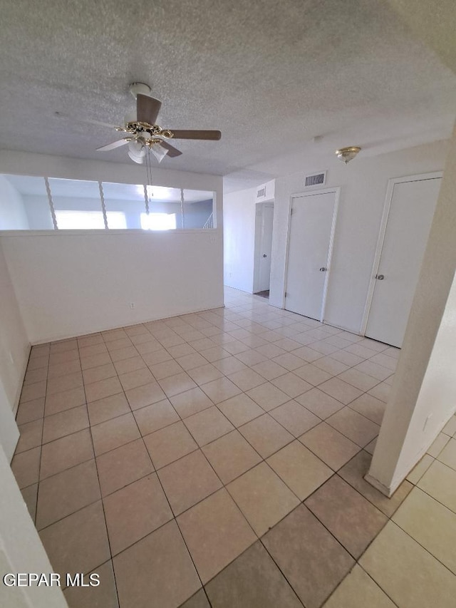 spare room featuring a ceiling fan, visible vents, a textured ceiling, and light tile patterned floors