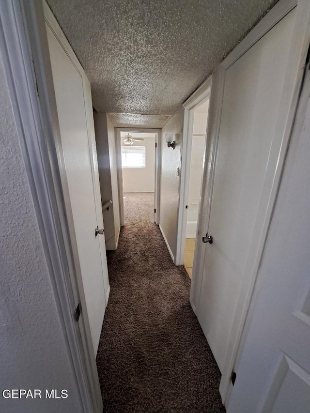 hall with a textured ceiling and dark colored carpet