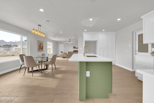 kitchen with a sink, white cabinets, light countertops, an island with sink, and pendant lighting