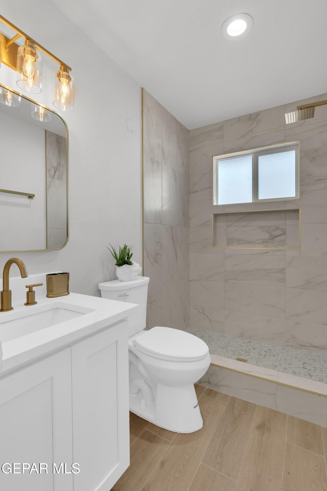 bathroom with tiled shower, vanity, toilet, and wood finished floors