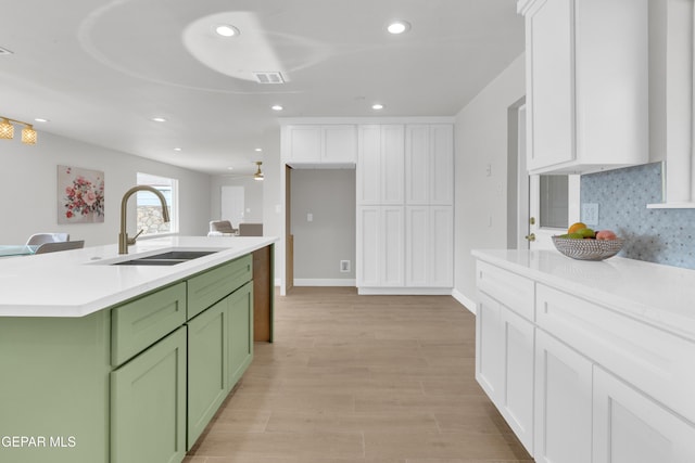 kitchen featuring light countertops, visible vents, green cabinets, a kitchen island with sink, and a sink