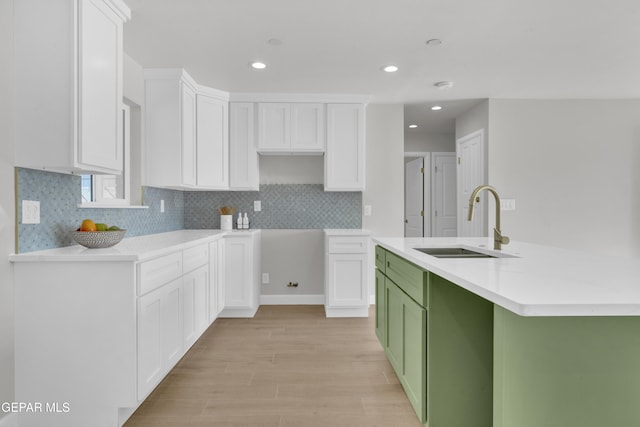 kitchen with light wood-style flooring, light countertops, white cabinetry, green cabinets, and a sink