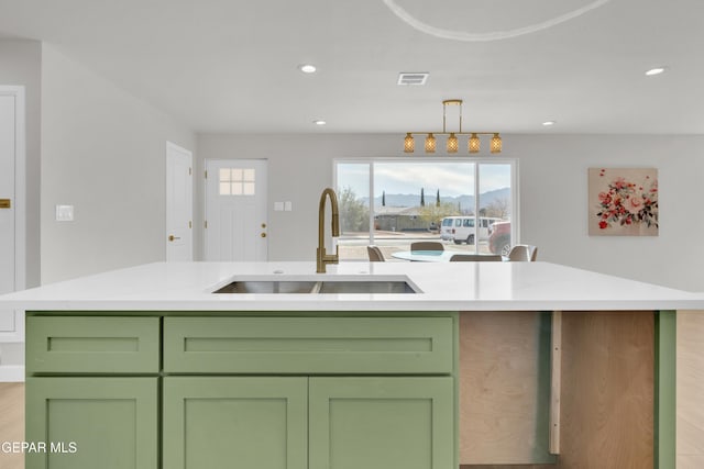 kitchen with light countertops, hanging light fixtures, visible vents, a sink, and an island with sink