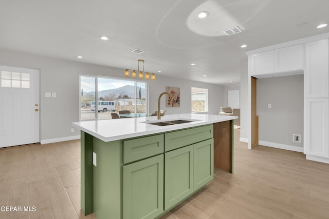 kitchen featuring a kitchen island with sink, a sink, visible vents, light countertops, and decorative light fixtures