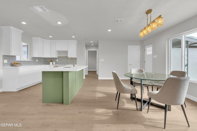 kitchen featuring white cabinetry, light countertops, hanging light fixtures, decorative backsplash, and a center island with sink