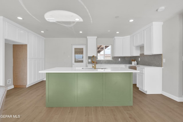 kitchen with a center island with sink, white cabinetry, light countertops, and a sink