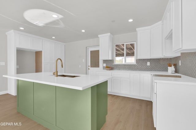 kitchen with a kitchen island with sink, white cabinets, a sink, and light countertops