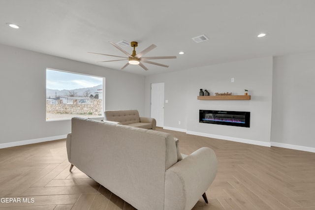 living room with visible vents, baseboards, a ceiling fan, a glass covered fireplace, and recessed lighting