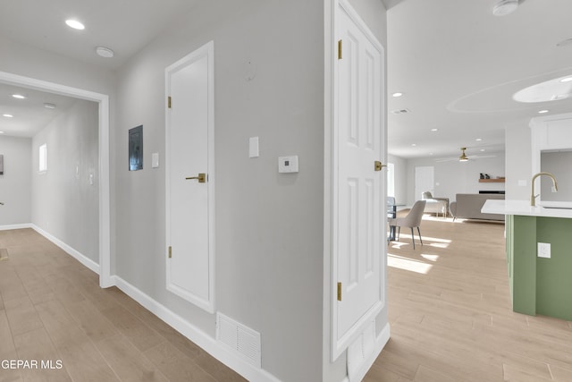 hall featuring recessed lighting, a sink, visible vents, baseboards, and light wood-type flooring