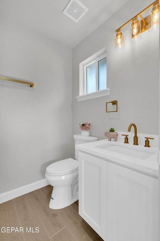 half bathroom with baseboards, visible vents, toilet, wood finished floors, and vanity