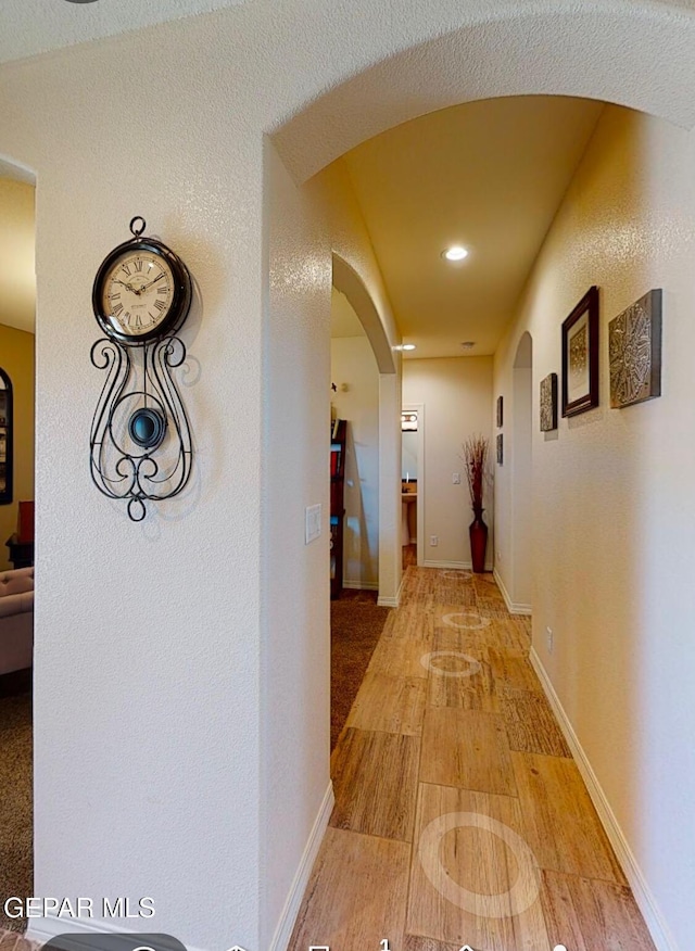 hall featuring arched walkways, light wood-type flooring, and baseboards