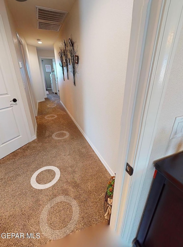 hall with baseboards, visible vents, and carpet flooring