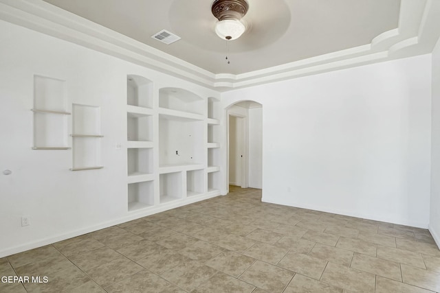 unfurnished room with visible vents, arched walkways, built in features, ceiling fan, and a tray ceiling