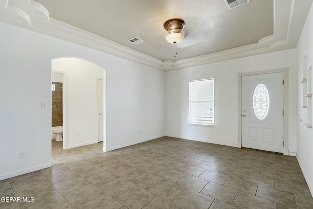 foyer entrance with arched walkways, a raised ceiling, visible vents, and baseboards