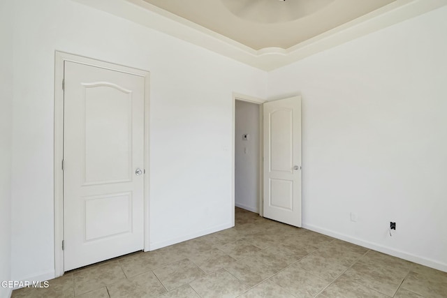 unfurnished bedroom featuring light tile patterned floors, baseboards, and a tray ceiling