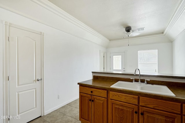 kitchen featuring dark countertops, light tile patterned floors, crown molding, and a sink