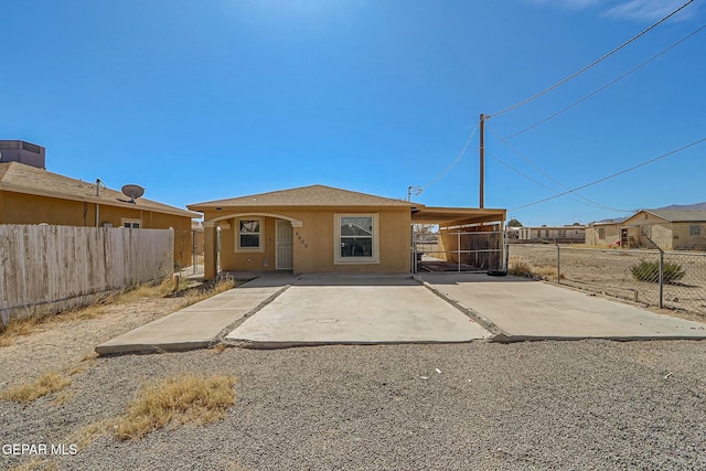 rear view of property with driveway, fence, an attached carport, and stucco siding