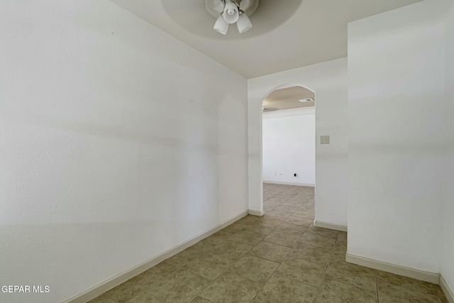 empty room featuring arched walkways, ceiling fan, baseboards, and light tile patterned floors