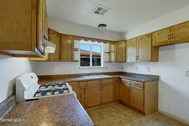 kitchen featuring white range with gas cooktop, visible vents, brown cabinetry, dark countertops, and a sink