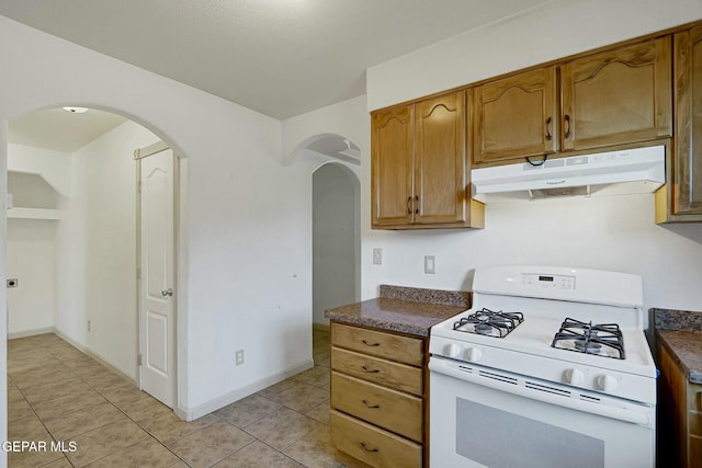 kitchen featuring under cabinet range hood, dark countertops, brown cabinets, and white range with gas cooktop