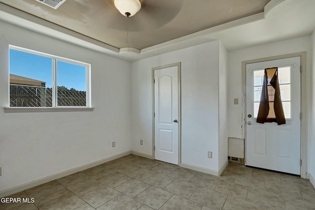 interior space with a raised ceiling, multiple windows, baseboards, and light tile patterned floors