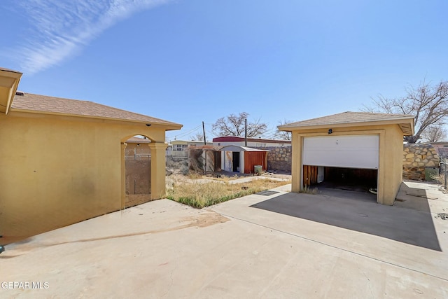 view of patio / terrace featuring a garage, an outdoor structure, driveway, and a storage shed