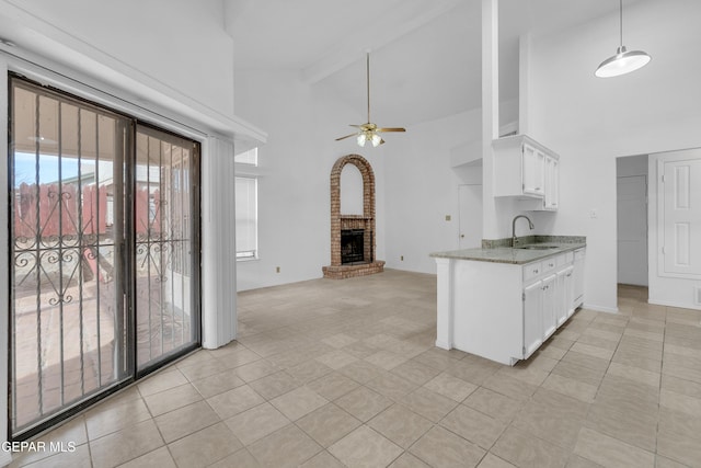 kitchen featuring light stone counters, a sink, white cabinets, open floor plan, and a brick fireplace