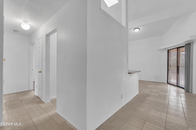 hall with a skylight, a textured ceiling, and light tile patterned floors