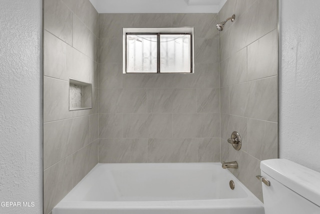 bathroom with toilet, shower / washtub combination, and a textured wall