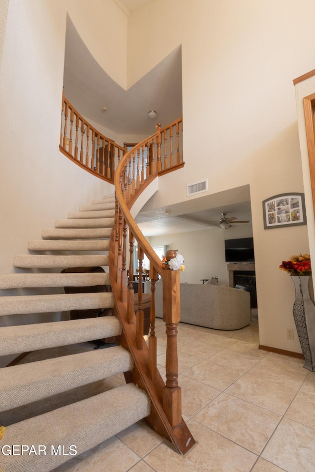 stairway with visible vents, a high ceiling, ceiling fan, baseboards, and tile patterned floors